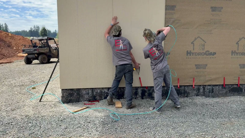 Two EZpanl crew members fastening a sheet of panel siding that is resting on a row of red EZpanl hooks along the foundation.