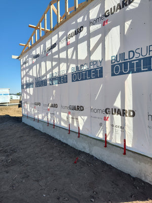 A row of red EZpanl siding hooks set along the base of a housewrapped wall, ready for the first panel.