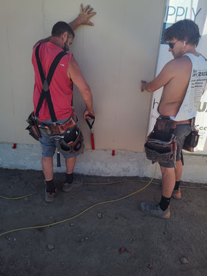 Two crew members resting a 4x8 siding panel on EZpanl hooks while they position it against the wall.