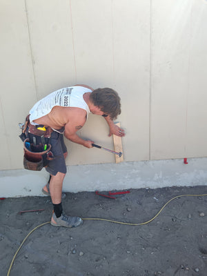 A crew member tapping an EZpanl hook free with a hammer and a block of wood after the panel is fastened, with two removed hooks on the ground.